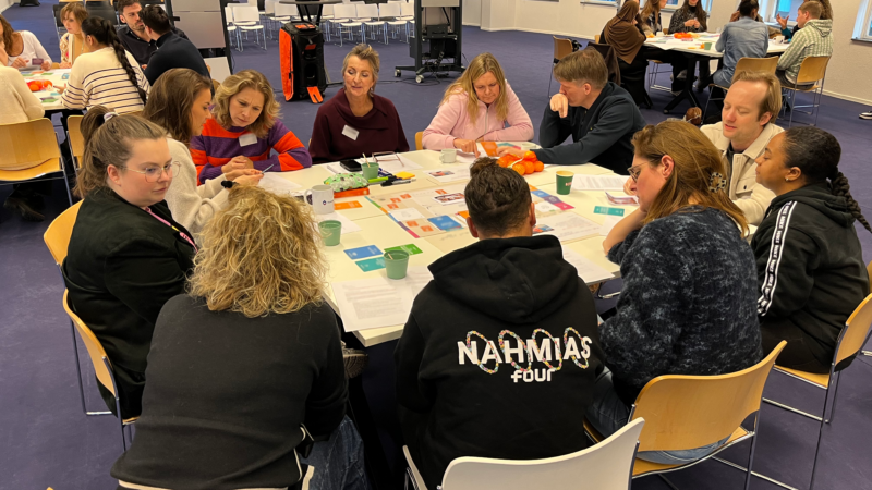 Een groep mensen om een tafel heen die het Optimaal Digitaal spelen tijdens een interactieve workshop bij ACM